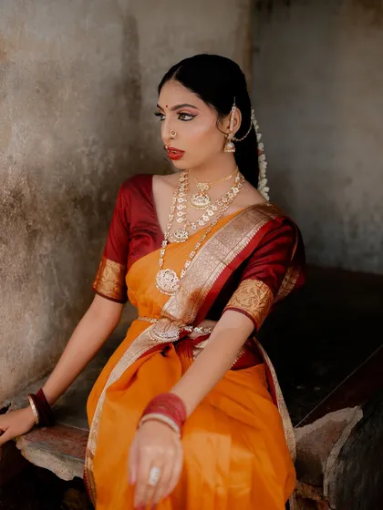 A seated portrait of a model in a traditional saree against a rustic wall. The soft, diffused light and her thoughtful expression create a peaceful and timeless image.