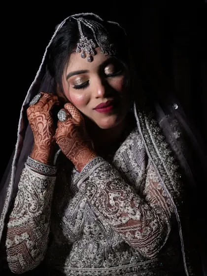 A close-up of a Muslim bride adjusting her earring, highlighting her intricate henna and beautiful makeup.