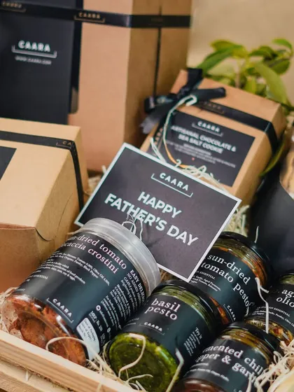 A close-up of our Father's Day hamper, packed in a rustic wooden crate. It includes a variety of his favourite things, from sun-dried tomato crostini and basil pesto to artisanal cookies and a 'Happy Father's Day' card.