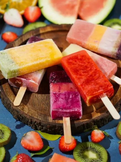 An assortment of colorful fruit popsicles on a wooden board, surrounded by the fresh fruits they are made from.