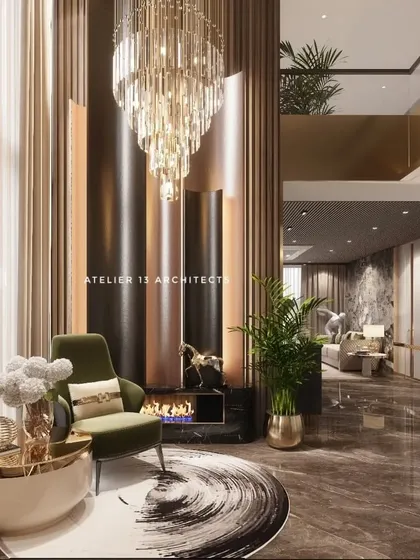 This dramatic corner of a living room features a fireplace set within a wall of fluted, metallic panels that rise to the double-height ceiling. A crystal chandelier and a plush green armchair create a cozy yet glamorous reading nook.