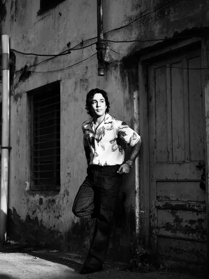 Zahan Kapoor leaning against a weathered wall. The textures of the setting and the soft lighting give this black and white photo a timeless, cinematic quality.