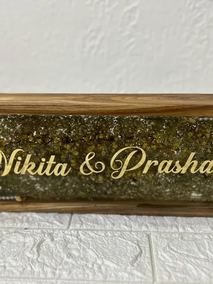 A beautiful wooden frame nameplate, filled with preserved green and yellow flowers. The couple's names in gold script stand out beautifully against the floral background.