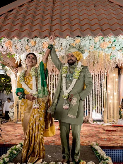 The couple celebrates under the mandap, their hands raised in joy.
