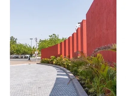 The exterior of the Glass Pavilion, featuring a bold, red, articulated wall that contrasts with the transparency of the main hall. This element serves as both a visual anchor and a guide for circulation.