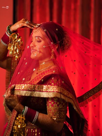 A beautiful portrait of the bride, her face softly lit in red. She adjusts her veil, creating a classic and graceful pose.