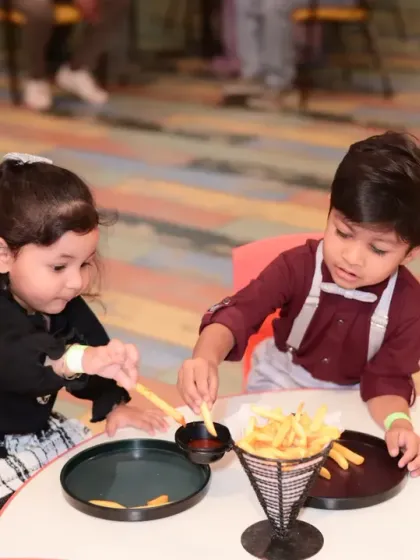 Two toddlers sharing a snack of french fries. Our menu includes treats that are perfect for little hands and appetites.
