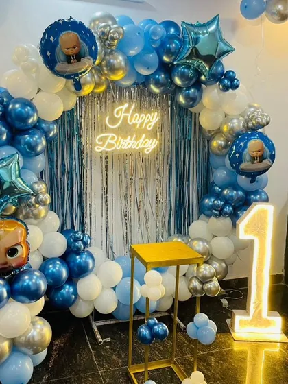 A classic Boss Baby themed birthday party setup. This decoration features a circular balloon arch in blue, white, and silver, a 'Happy Birthday' neon sign, and character foil balloons.