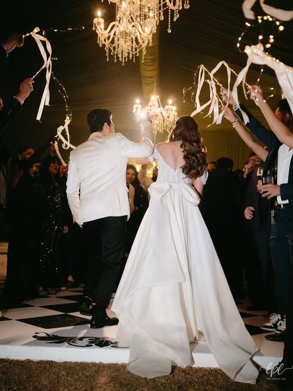 The couple shares their first dance on a custom checkered dance floor, surrounded by guests under the warm glow of crystal chandeliers.