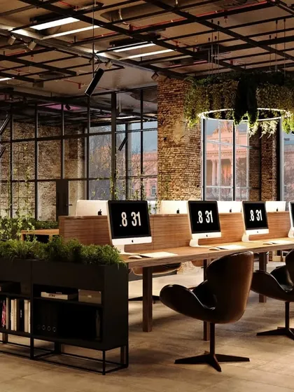 This industrial-style open office combines raw materials like exposed brick and metal grid ceilings with warm wood and lush greenery. The layout promotes collaboration with long communal desks, while the aesthetic reflects a modern, creative, and dynamic company culture.