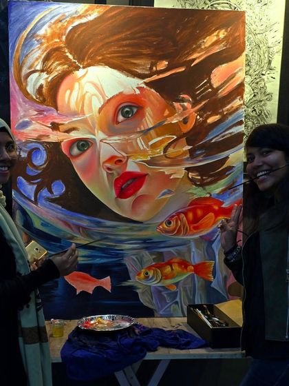 A happy moment in the studio. Two students pose with a large, surrealist oil painting of a face submerged in water, a collaborative and imaginative project.