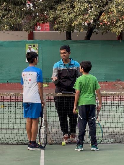 A coach providing tactical advice to two young players by the net. These strategy sessions are just as important as the physical drills.