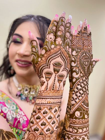 A happy client showing off her unique Karva Chauth mehandi, which features kalash or pot motifs on the back of her hands.