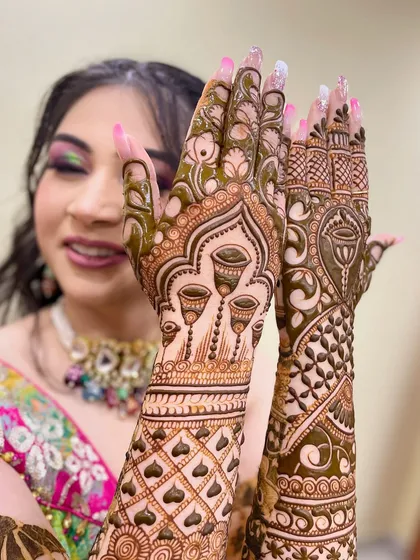 A happy bride showing off her unique mehandi, which features hanging kalash motifs.