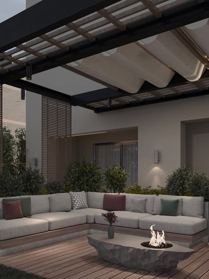 As dusk settles, the lighting in this outdoor lounge creates a warm and inviting ambiance. The design includes wall sconces, a modern floor lamp, and the glow from the fire pit, all contributing to a magical atmosphere.