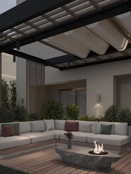 As dusk settles, the lighting in this outdoor lounge creates a warm and inviting ambiance. The design includes wall sconces, a modern floor lamp, and the glow from the fire pit, all contributing to a magical atmosphere.