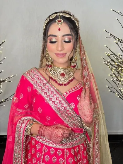 A lovely bride in a bright pink lehenga. Her makeup is fresh and glowing, with a beautiful red bindi and matching jewelry.