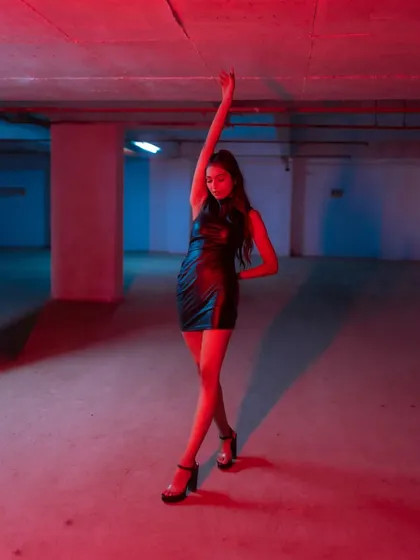 A full-body shot capturing a graceful, dance-like pose under dramatic red lighting in an empty parking garage.