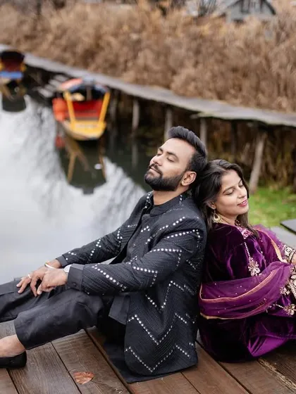 A peaceful and reflective portrait of the couple sitting back-to-back on a wooden dock at Dal Lake. This image captures a quiet moment of togetherness amidst the stunning natural beauty of Kashmir.