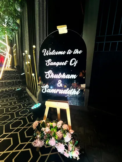 A personalized acrylic welcome sign with neon-style lettering, placed at the entrance of the Sangeet to greet guests.