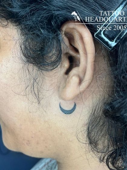 A tiny crescent moon tattoo placed discreetly behind the ear.