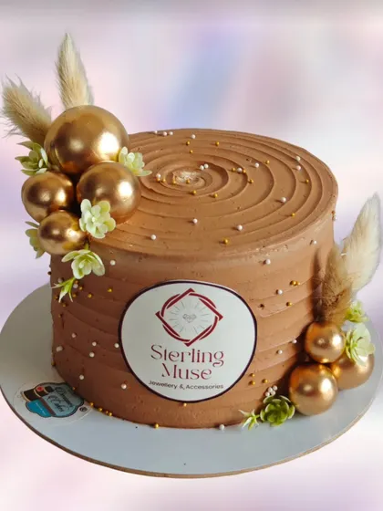 A corporate cake with a wood grain texture and a printed logo. The gold spheres and dried pampas grass add a touch of rustic elegance.