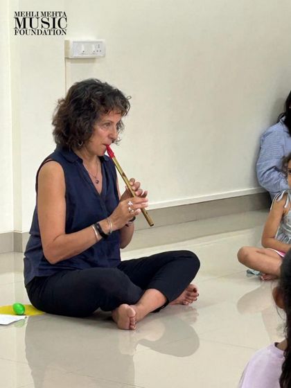 An instructor demonstrates a wind instrument to a captivated group of young students. Introducing various instruments sparks curiosity and helps children understand different ways of making music.