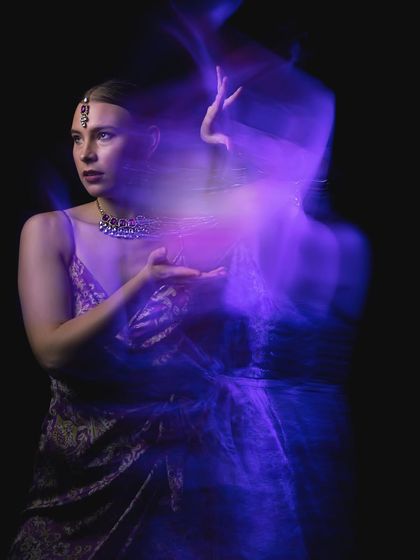 An experimental portrait using slow shutter speed and light painting to create a purple, ethereal ghost-like effect around a model in traditional attire.