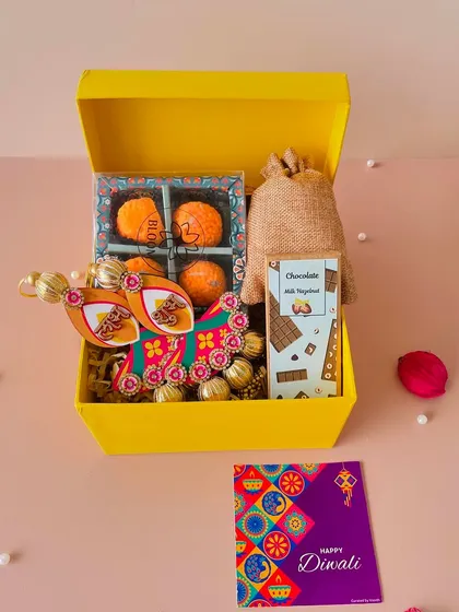 This bright yellow box is a cheerful choice for Diwali. It's filled with laddoo candles, Shubh Labh door hangings, a chocolate bar, and a potli of almonds.