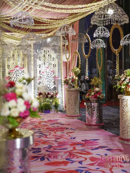 The grand entryway, featuring a pink floral carpet runner lined with flower-topped pedestals. The ceiling is adorned with hanging crystal umbrellas and draped fabrics, creating a magical first impression.