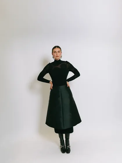 A full-length studio shot for Tululs against a clean white background. The simple, elegant styling and confident pose create a classic and sophisticated fashion portrait.