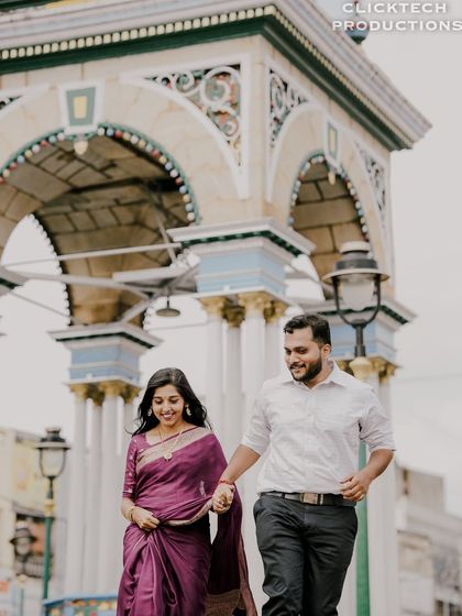 A happy, candid walking shot of a couple in traditional wear, with a classic city archway in the background.