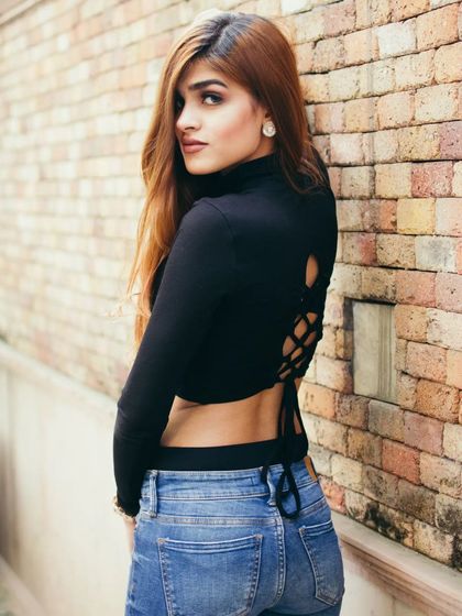 A casual street style portrait against a brick wall, showcasing a relaxed and confident pose. The natural light and simple setting keep the focus entirely on the subject's personality.