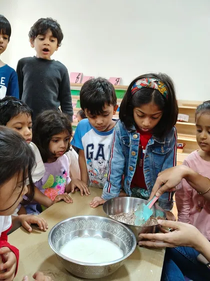 Learning is delicious. Here, children are gathered for a group baking activity, watching intently as ingredients are mixed. This practical life lesson teaches them about measurement, following instructions, and the science of cooking.