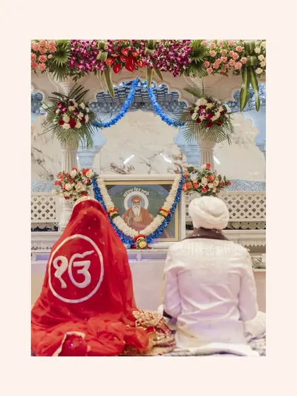 A serene moment from an Anand Karaj ceremony, with the couple seated before a portrait of Guru Ram Das, symbolizing a blessed union.