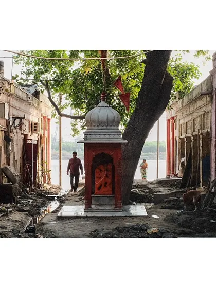 The aftermath of a flood on the ghats of the Yamuna River. A small shrine stands resiliently amidst the mud and debris, a symbol of enduring faith.