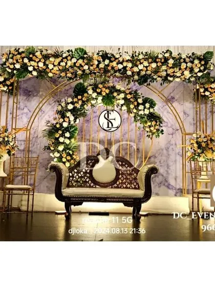 This elegant reception stage uses a soft, marbled backdrop with gold framework and lush white and green florals. The design is both modern and timeless, suitable for a sophisticated wedding celebration.