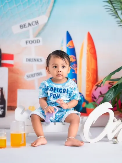 A classic portrait from a beach-themed milestone session. The setup includes "One" lettering to mark the special occasion alongside fun, tropical props.