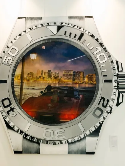 The nighttime view of the lenticular artwork 'Mumbai in Motion.' This image shows the city skyline illuminated, with a red sports car driving along the waterfront, all within the face of a watch.