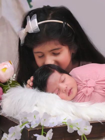 A sweet moment between an older sister and her newborn sibling in a bohemian-themed setup. The soft lighting and floral props add to the gentle mood.