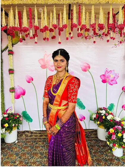 The bride posing against a beautiful floral backdrop during her Pellikuthuru. Her purple and red saree combination is so vibrant and joyful.