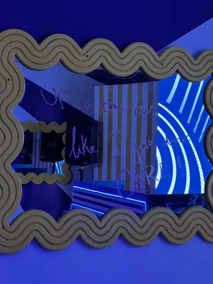 A quirky, wave-edged mirror reflecting the party's vibrant blue lighting and striped decor. Guests could write messages on the mirror, adding an interactive and personal element to the event.
