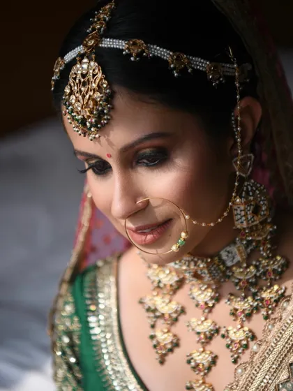 An intricate bridal look featuring heavy Polki jewellery with green accents. The eye makeup is a dramatic smokey look, balanced with a neutral lip color to let the jewellery stand out.