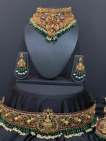 This choker set features intricate temple work with green bead detailing. It comes with a matching vaddanam, maang tikka, and earrings for a complete look.