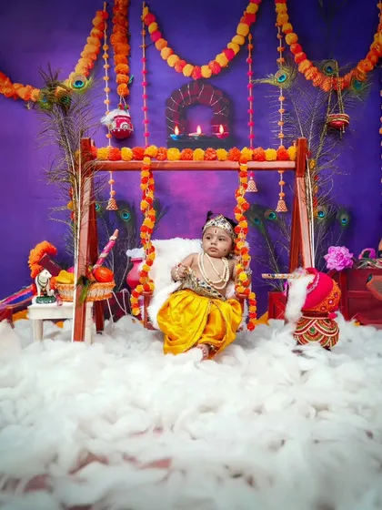 A full view of the Radha theme setup, with a beautiful swing decorated with marigold garlands and peacock feathers against a rich, festive background.