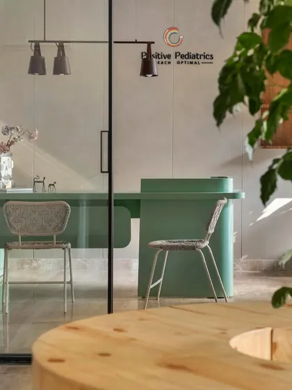 The doctor's consultation room is designed to be calm and reassuring. A clean, mint-green desk and simple woven chairs create a professional yet approachable atmosphere, viewed through a sleek glass partition.