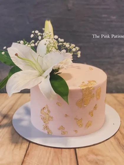 A minimalist pink cake with gold leaf accents and a single, stunning white lily. This design is all about simple elegance.