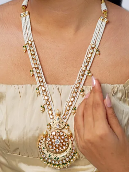 A beautiful long necklace, or rani haar, featuring a large kundan pendant and pearl strings. This piece can be layered with a choker or worn on its own for an elegant, royal look.