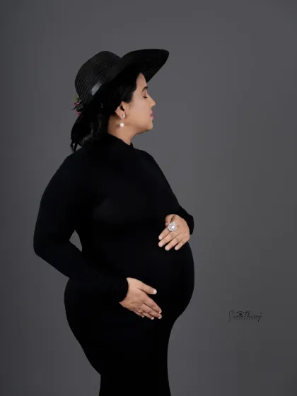 A classic profile shot of a mother-to-be in a black gown and hat. The simple grey background and elegant pose create a timeless and sophisticated portrait.