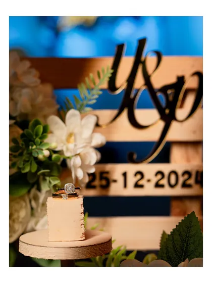 A macro shot of the engagement ring, elegantly placed on a decorative stand with the couple's initials and wedding date in the background.